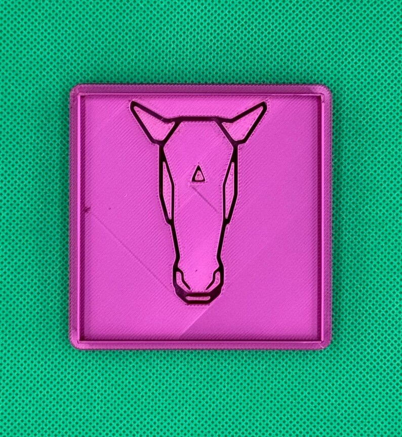 K&ouml;nnte beinhalten: Eine rosa Plastikplakette mit einer schwarzen Umrandung eines Pferdekopfes.
