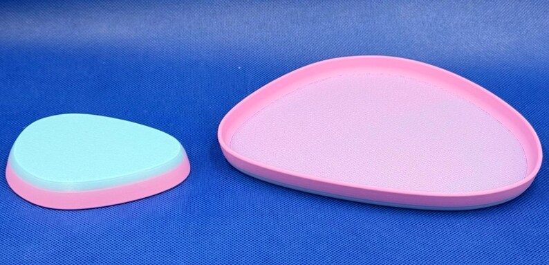 May include: Two pastel-colored, oval-shaped serving trays. The larger tray is pink with a light blue rim. The smaller tray is light blue with a pink rim.