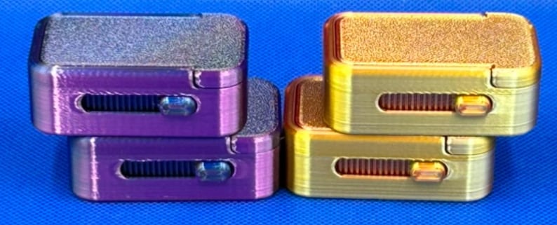 May include: Two stacks of rectangular fidget sliders, one stack in metallic purple and the other in metallic gold. Each slider features a textured top surface, a horizontal grooved track, and a small sliding button on the front face.