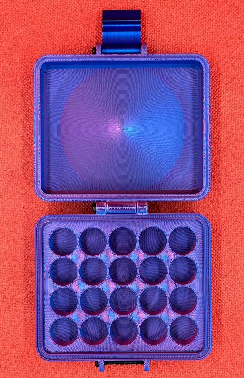 May include: A rectangular, hinged storage case with a vibrant blue and purple gradient finish. The top section is an open, empty compartment, while the bottom section features a grid of sixteen circular cutouts for organising small items.
