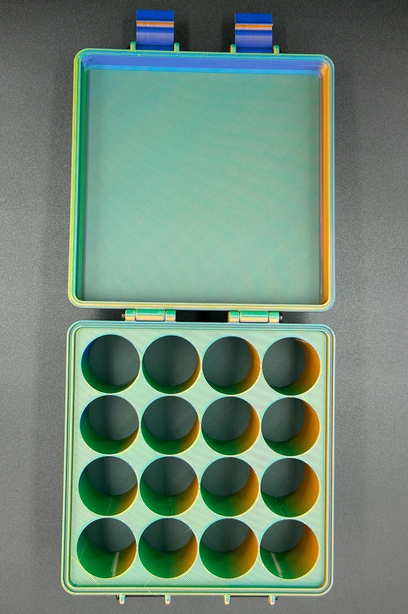 May include: A green and orange plastic storage box with a hinged lid and 15 round compartments. The box is open and the lid is propped up.
