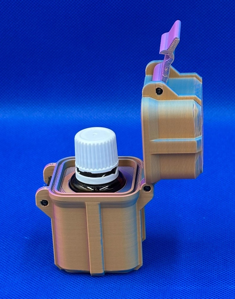 May include: A tan, rectangular, 3D-printed storage case with a hinged lid standing open. Inside the case sits a small, dark amber glass bottle with a white, ribbed, screw-top cap. The case features vertical ridges and a latch mechanism.