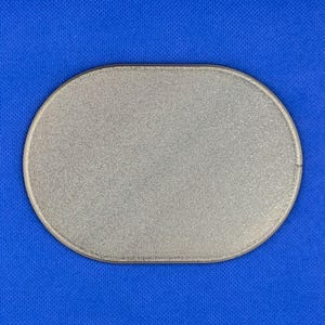 May include: A silver-colored oval patch with a textured, glittery surface and a stitched border. The object features a uniform metallic finish across its entire front face, presenting a clean, simple shape with rounded edges and a flat profile.