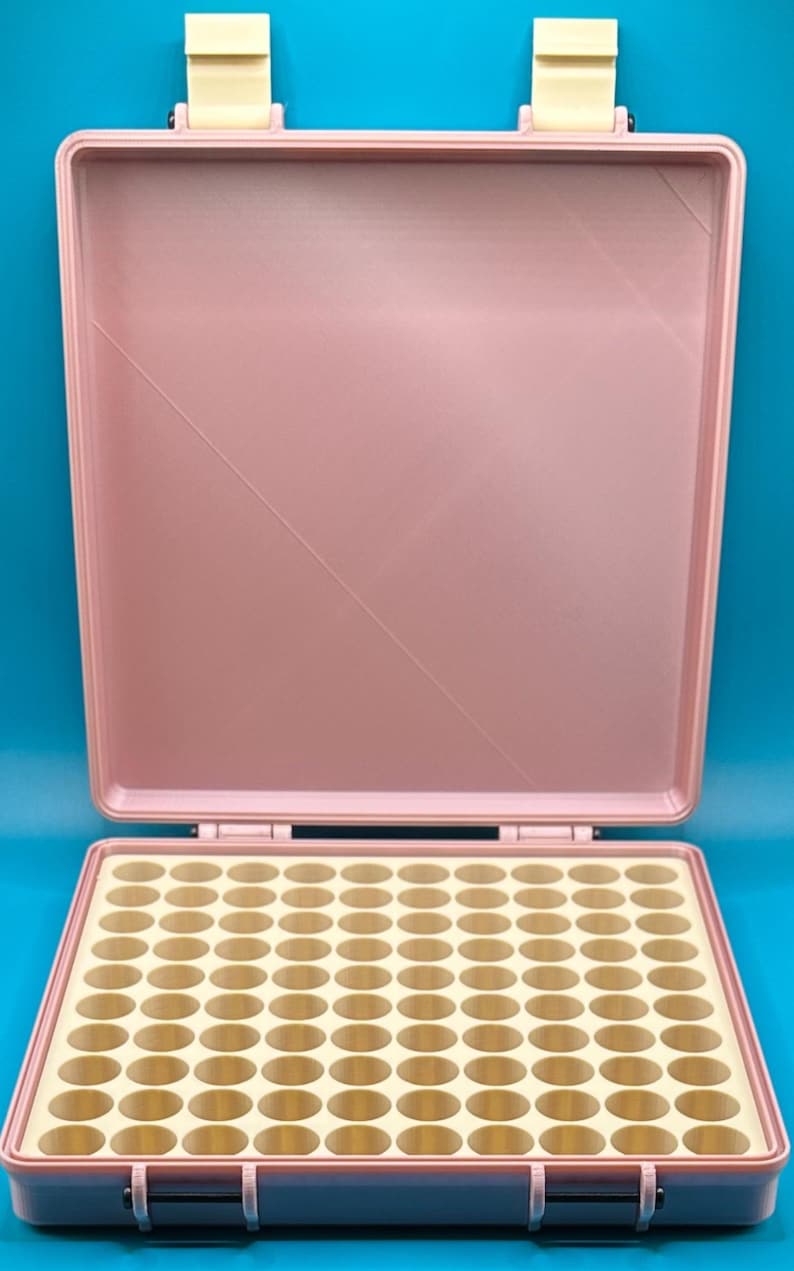 May include: A pink plastic storage case with a removable lid and a grid of 50 round compartments. The case is open and the compartments are empty.