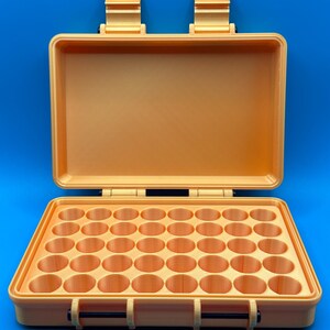 May include: A rectangular, light orange storage case with an open lid and two top hinges. The interior base features a grid of forty circular compartments arranged in five rows of eight, designed for holding small cylindrical items securely.