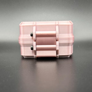 May include: A light pink, rectangular, 3D-printed storage box featuring a hinged lid mechanism. The container has a smooth, layered texture and is secured with two small, dark metal screws visible on the side hinge assembly.