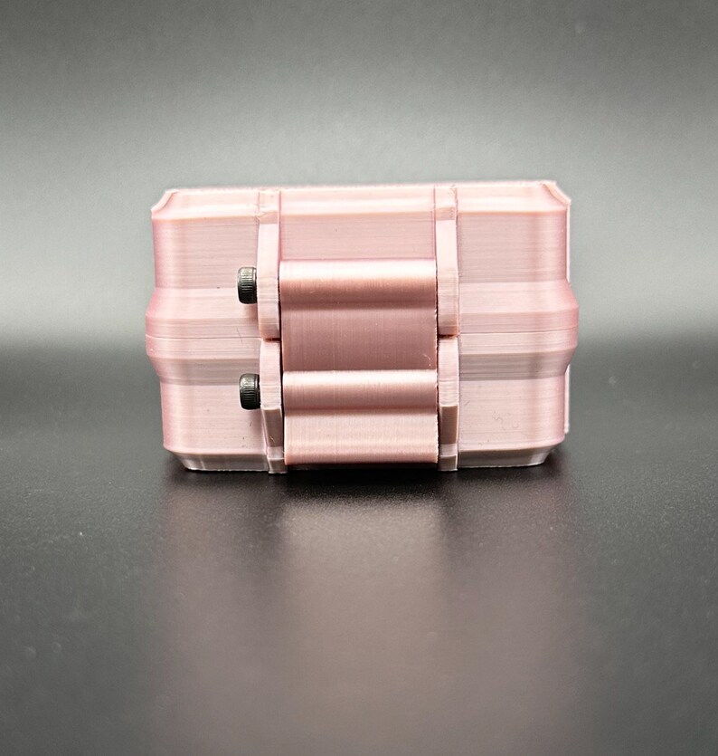 May include: A light pink, rectangular, 3D-printed storage box featuring a hinged lid mechanism. The container has a smooth, layered texture and is secured with two small, dark metal screws visible on the side hinge assembly.