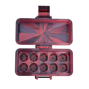 May include: A rectangular, hinged storage case with a red and black marbled finish. The interior lid features a starburst pattern, while the base contains ten circular compartments, each with a matching starburst design at the bottom.