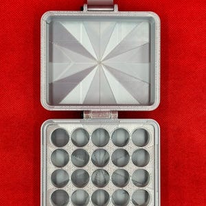 May include: A light grey, rectangular, 3D-printed storage case with a hinged lid. The interior of the lid features a sunburst pattern, while the base contains twenty circular compartments arranged in a four-by-five grid for small items.