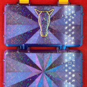 May include: Two purple and blue iridescent plastic cases with a starburst pattern. The top case has a gold outline of a horse's head.