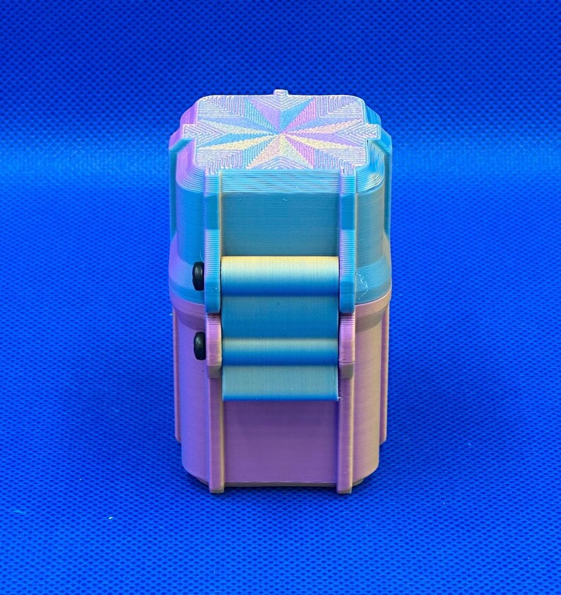 May include: A small, rectangular, 3D-printed storage container with a hinged lid. The object features a gradient color scheme transitioning from light blue at the top to a soft pink at the base, with a geometric star pattern on the lid.