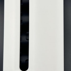May include: A white rectangular dispenser featuring a vertical black viewing slot in the center. The unit includes a bright red cap at the top and a matching red circular component protruding from the bottom right side.