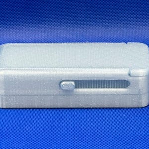 May include: A rectangular, silver-colored storage box with a glittery finish. The box features a sliding latch mechanism on the front side, which is positioned within a horizontal recessed track. The lid is flat and the edges are rounded.