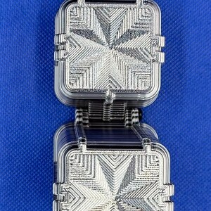 May include: A dual-layered square object featuring a clear, transparent plastic construction with a detailed, embossed geometric star pattern on the top surfaces. The item has a stacked design with visible ribbed edges and a dark, striped connector.