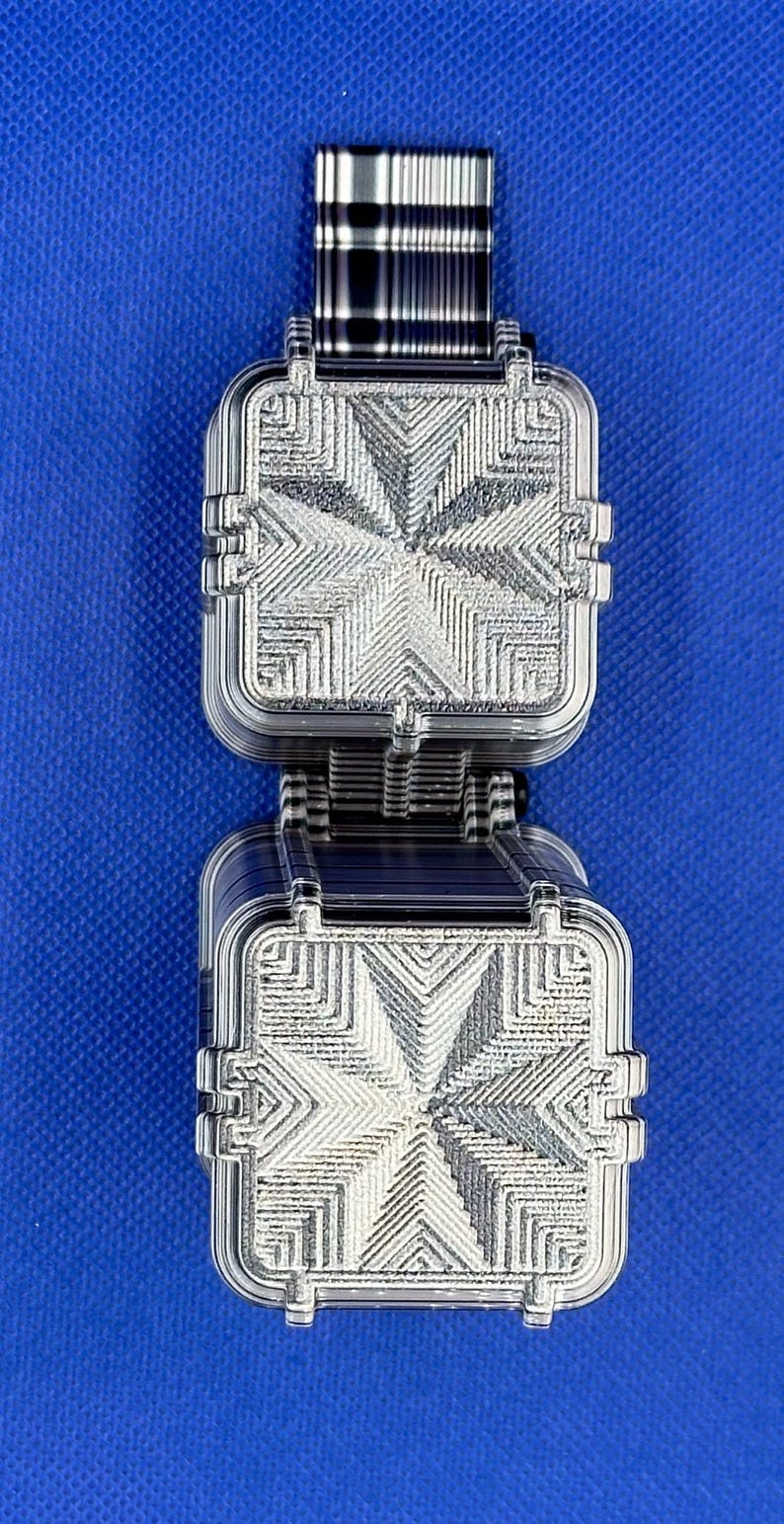May include: A dual-layered square object featuring a clear, transparent plastic construction with a detailed, embossed geometric star pattern on the top surfaces. The item has a stacked design with visible ribbed edges and a dark, striped connector.