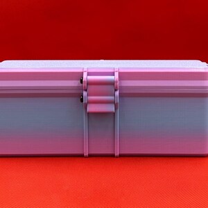 May include: A rectangular storage box featuring a gradient color scheme that transitions from light purple at the top to a soft blue at the base. The container includes a central latch mechanism with two small black pins and a textured lid surface.