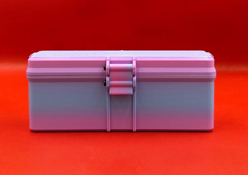 May include: A rectangular storage box featuring a gradient color scheme that transitions from light purple at the top to a soft blue at the base. The container includes a central latch mechanism with two small black pins and a textured lid surface.