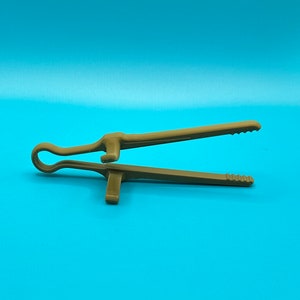 May include: A brown plastic kitchen tong tool featuring a looped handle at one end and two long, straight arms with serrated, gripping tips. The design includes a small, perpendicular support tab on each arm to keep the tool elevated.