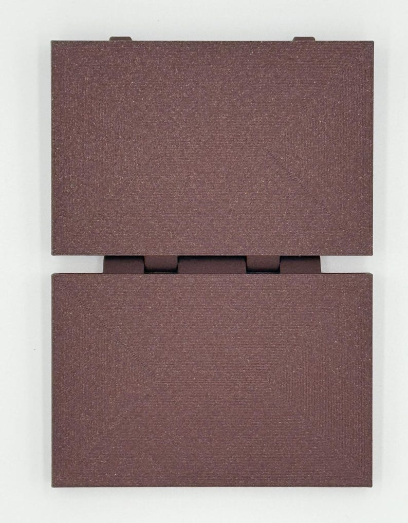 May include: Two rectangular, dark brown panels connected by hinges. The panels have a textured surface and are positioned vertically, with one panel slightly above the other. The color is a deep, earthy tone, suggesting a natural material.