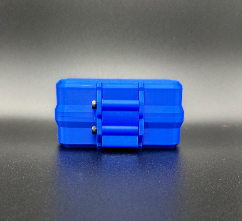 May include: A rectangular blue storage case featuring a hinged lid with a central latch mechanism. The case has a textured, rigid exterior with two small silver-colored metal pins visible on the side of the hinge assembly.
