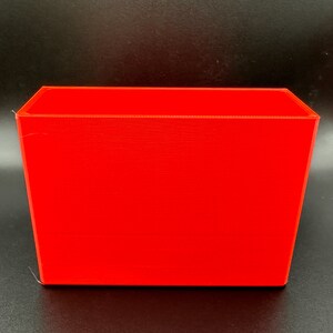 May include: A bright red rectangular plastic container. The container is empty and has a smooth surface.