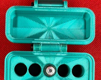 May include: A teal 3D-printed rectangular storage case with a hinged lid. The interior base features four circular compartments and one central cylindrical slot containing a small metal component with a circular opening.