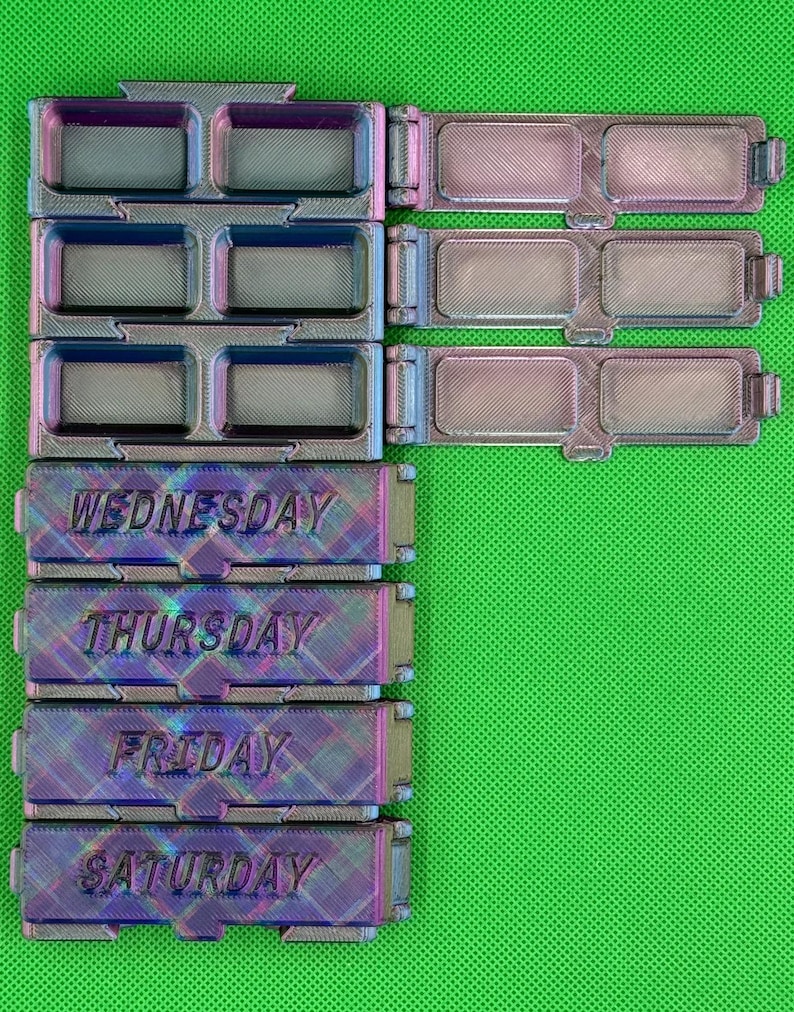 May include: A set of iridescent, multi-colored 3D printed pill organizers with hinged lids. The containers are labeled with the days of the week, specifically Wednesday, Thursday, Friday, and Saturday, featuring rectangular compartments for daily medication storage.
