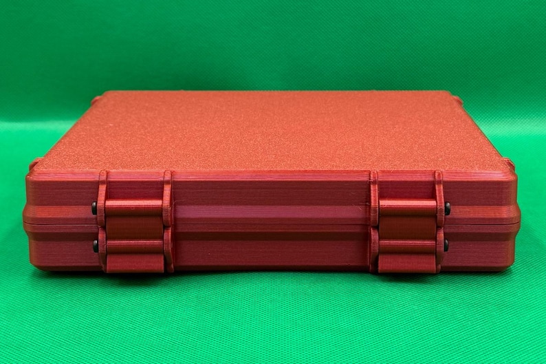 May include: A red rectangular storage case with a textured surface and two black hinges on each side.