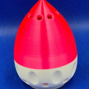 May include: A pink and white 3D printed object shaped like a teardrop with holes on the top and bottom.