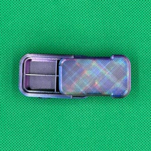 May include: A small, rectangular, iridescent pill case with a hinged lid. The case is divided into four compartments and has a textured, multi-colored finish. The open lid reveals the interior compartments, designed for organizing medication or small items.