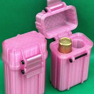 Puede incluir: Dos estuches de almacenamiento rectangulares de color rosa brillante con crestas verticales y pasadores de bisagra negros. Un estuche est&aacute; cerrado, mientras que el otro est&aacute; abierto, revelando un objeto cil&iacute;ndrico dorado.