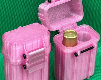 May include: Two rectangular, glittery pink storage cases with vertical ridges and black hinge pins. One case is closed, while the other is open, revealing a gold-colored cylindrical object inside a circular compartment next to an empty slot.