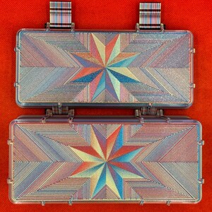 Puede incluir: Dos cajas de almacenamiento rectangulares con tapas abatibles, con un vibrante patr&oacute;n de estrella geom&eacute;trica multicolor en tonos azul, naranja y amarillo. Las cajas tienen una superficie lineal texturizada y dos pesta&ntilde;as a rayas en el borde superior.