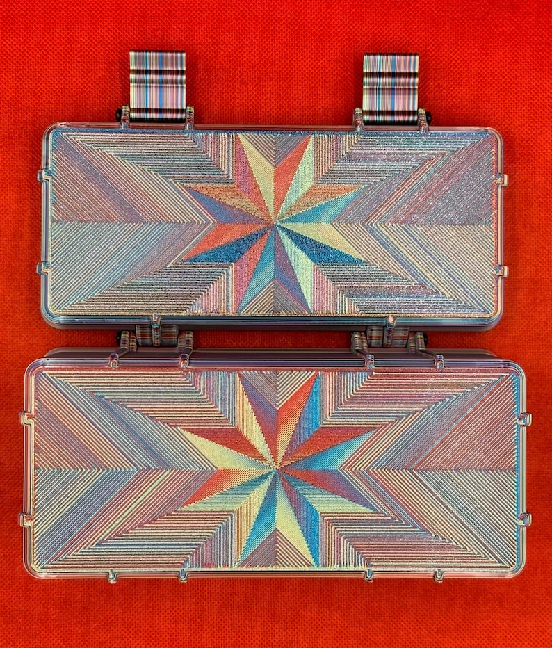 Puede incluir: Dos cajas de almacenamiento rectangulares con tapas abatibles, con un vibrante patr&oacute;n de estrella geom&eacute;trica multicolor en tonos azul, naranja y amarillo. Las cajas tienen una superficie lineal texturizada y dos pesta&ntilde;as a rayas en el borde superior.