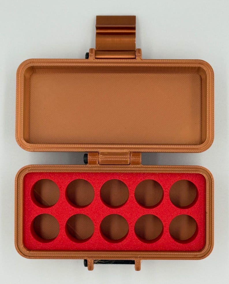 May include: A rectangular copper-colored plastic storage case with a hinged lid. The interior base features a bright red foam insert with ten circular cutouts arranged in two rows of five, designed for holding small cylindrical items.