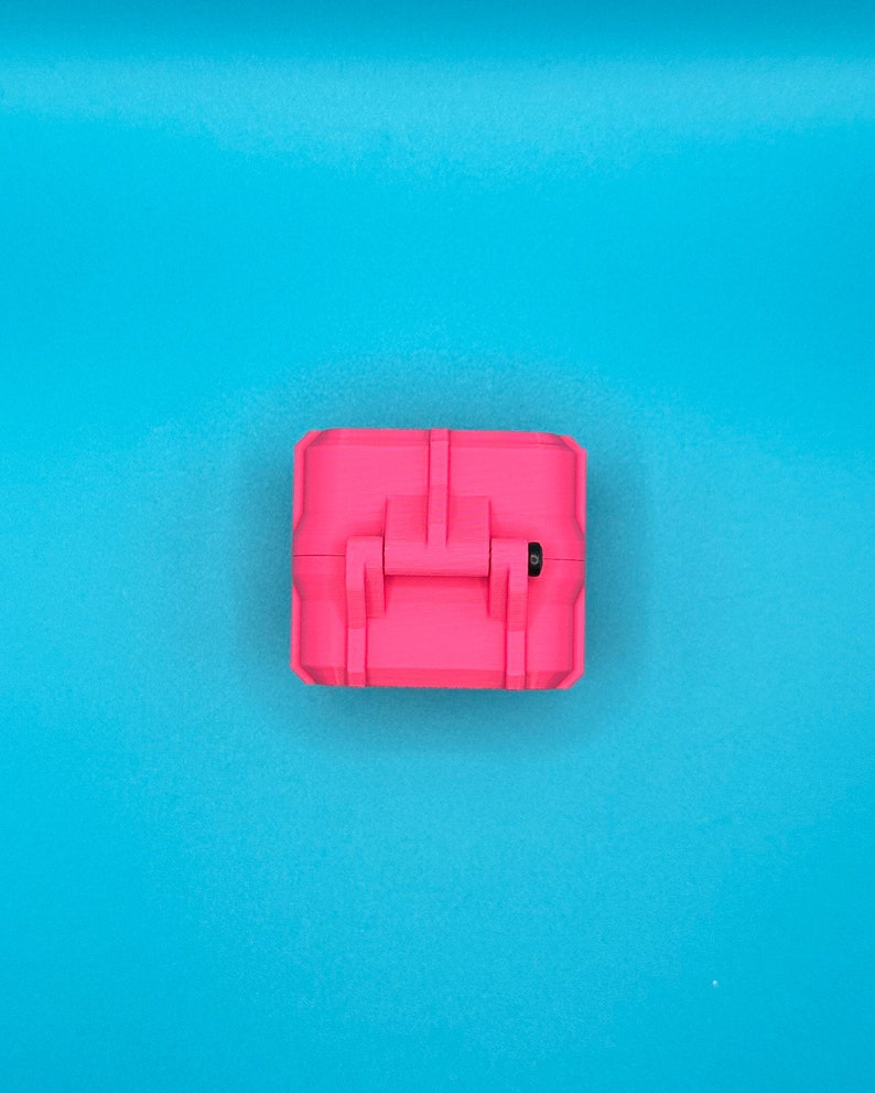 May include: A bright neon pink rectangular storage case with a hinged lid and a central latch mechanism. The case features a textured, matte finish and a small black circular detail visible near the hinge on the right side of the container.