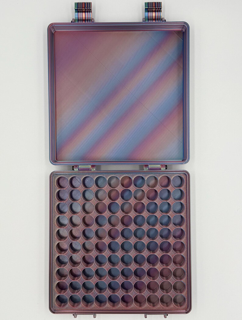May include: A square, open storage case featuring a gradient of iridescent purple, blue, and copper tones. The interior base contains a grid of eighty-one circular compartments, while the lid is smooth with a matching multi-colored finish.
