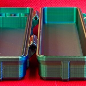 May include: A two-piece, teal and blue, plastic storage case with a latching lid and a small compartment on one side.