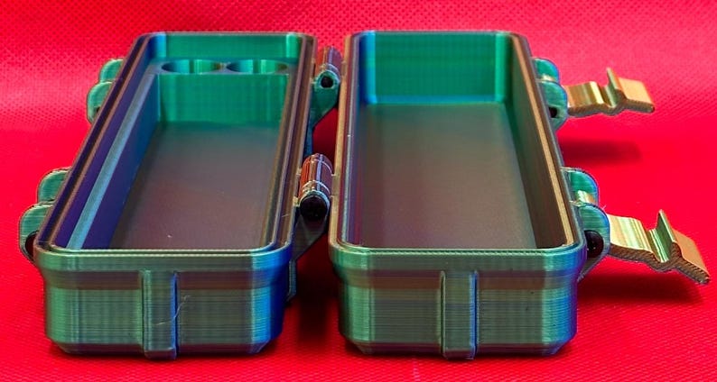May include: A two-piece, teal and blue, plastic storage case with a latching lid and a small compartment on one side.