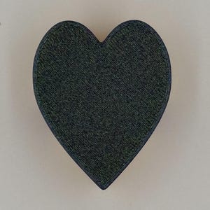 May include: A dark green heart-shaped object with a textured surface and a dark blue outline. The heart is centered against a light beige background. The object appears to be made of a solid material.