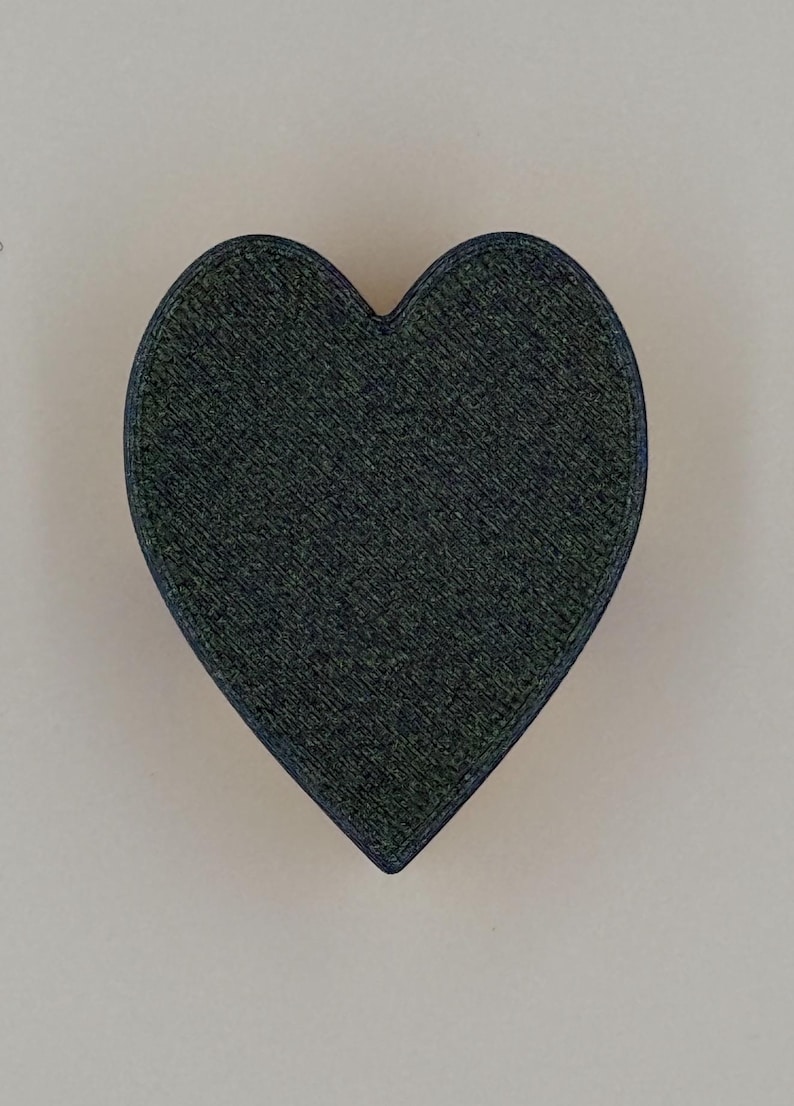 May include: A dark green heart-shaped object with a textured surface and a dark blue outline. The heart is centered against a light beige background. The object appears to be made of a solid material.