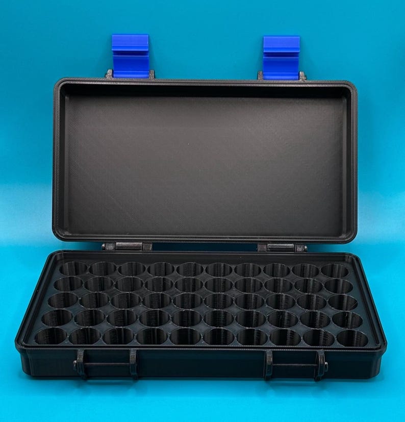 May include: A black rectangular storage case with a hinged lid and two bright blue latches. The interior features a grid of forty-eight circular compartments arranged in six rows of eight, designed for organising small cylindrical items.