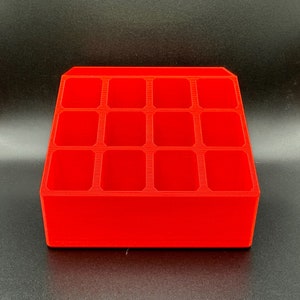 May include: A bright red plastic organizer with twelve rectangular compartments. The organizer is designed to hold small items, such as craft supplies or jewelry.