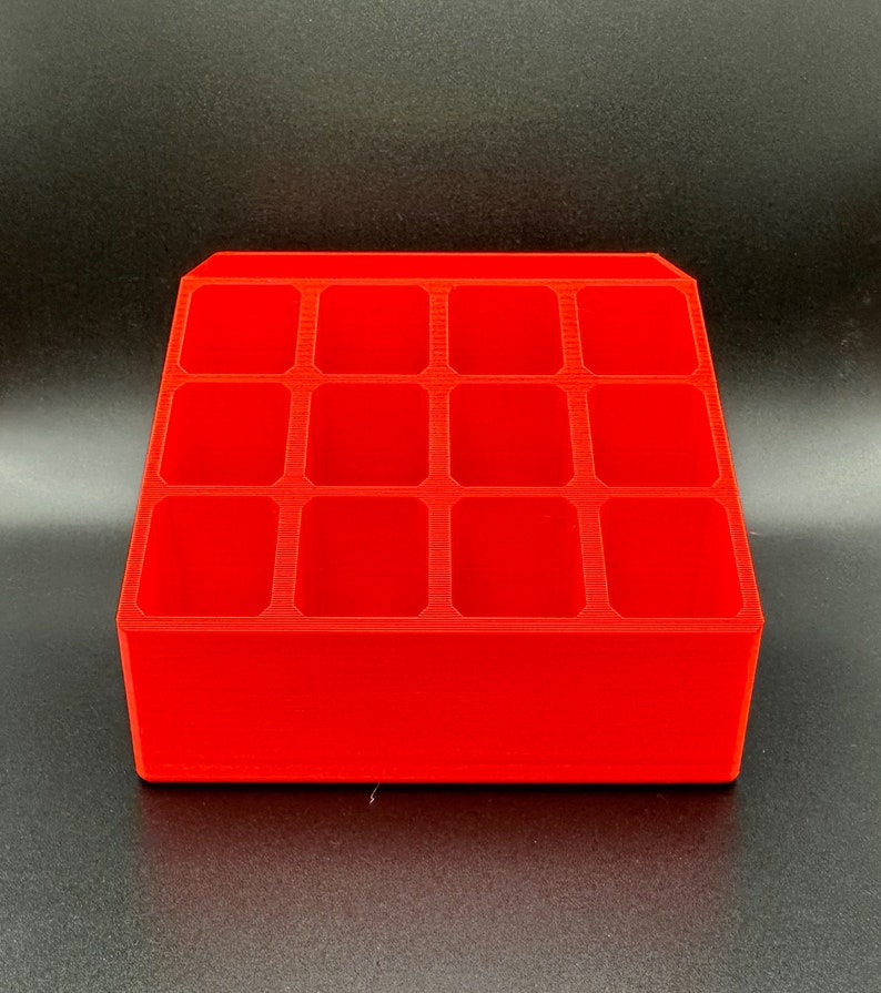 May include: A bright red plastic organizer with twelve rectangular compartments. The organizer is designed to hold small items, such as craft supplies or jewelry.