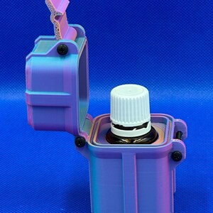 May include: A 3D-printed, rectangular storage case with a hinged lid, featuring a gradient of purple and blue colors. The case is open, revealing a small amber glass bottle with a white ribbed cap seated securely inside the central compartment.