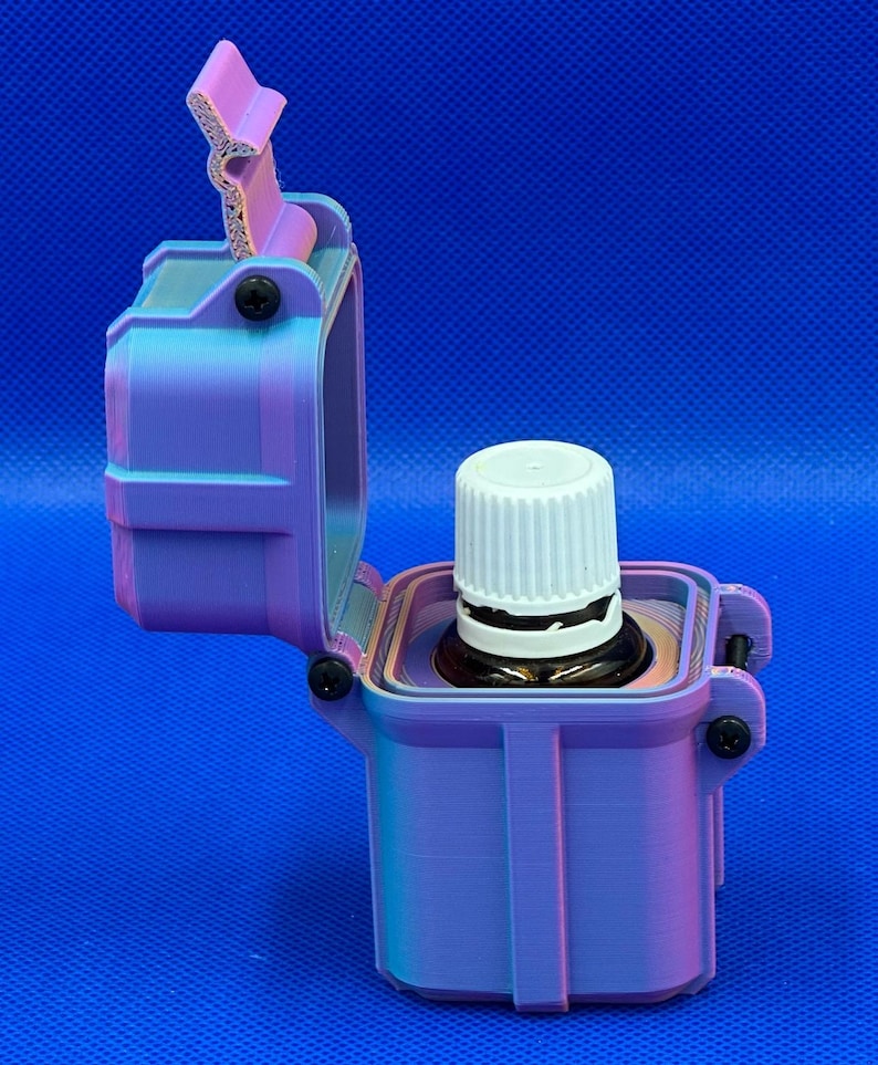 May include: A 3D-printed, rectangular storage case with a hinged lid, featuring a gradient of purple and blue colors. The case is open, revealing a small amber glass bottle with a white ribbed cap seated securely inside the central compartment.
