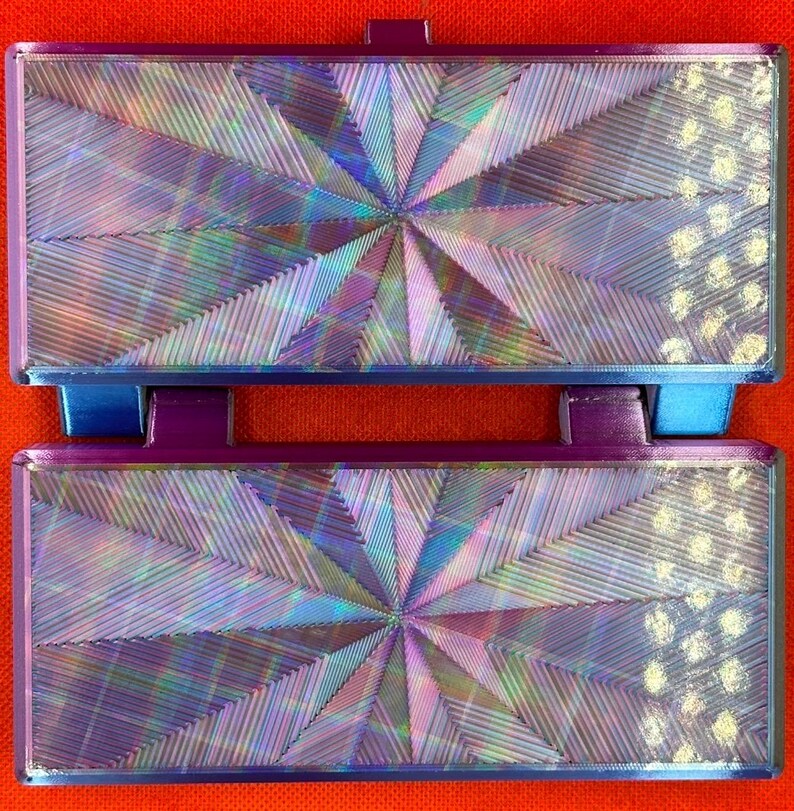 May include: Two rectangular, hinged components featuring a vibrant, iridescent finish with a central starburst pattern of fine, radiating lines. The edges are framed in a deep purple, and the right side displays a textured, dotted pattern.