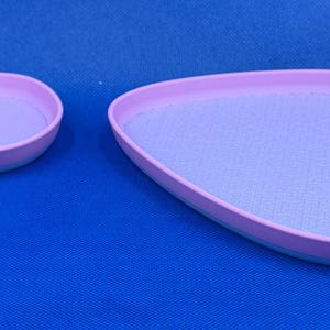 May include: Two light purple oval-shaped trays with a light blue rim. The larger tray is slightly wider than the smaller tray.