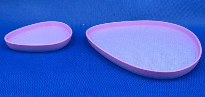 May include: Two light purple oval-shaped trays with a light blue rim. The larger tray is slightly wider than the smaller tray.