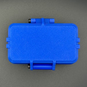 May include: A rectangular blue storage case with a textured surface and rounded corners. The case features a hinged lid mechanism with visible black metal screws on the side hinges, providing a secure closure for the container.